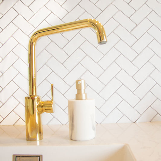 Hvid peel and stick flise (snowbone) fra stickoramic i sildebensmønster. Brugt som backsplash i køkken med hvid håndvask og guld vandhane.