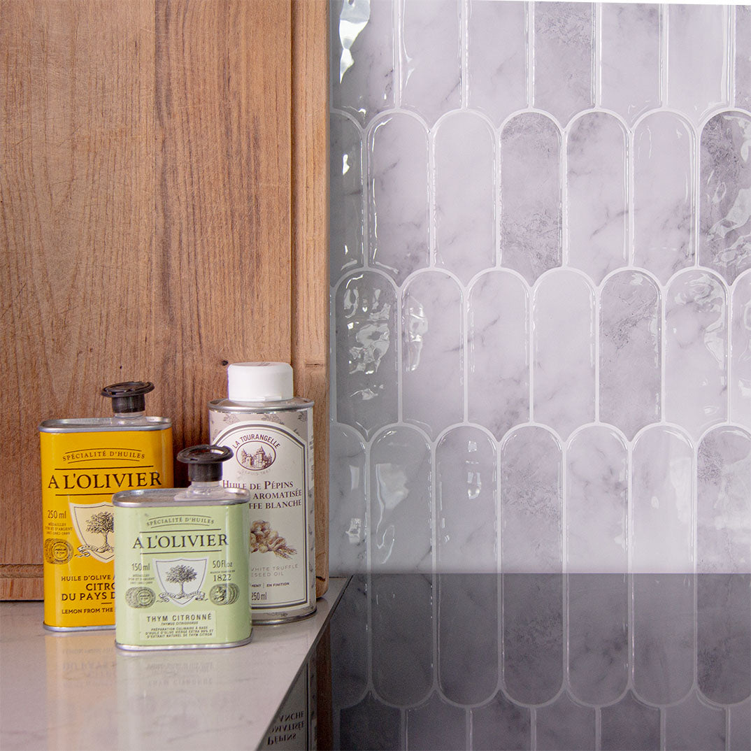 Marmorlignende fliseklistermærker i mønster med lodrette ovale stave op mod komfor pyntet med skærebræt og olier.