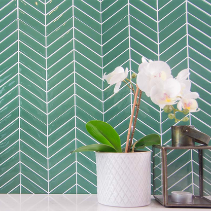 Grønne fliseklistermærker i chevron mønster i bryggers med hvid bordplade pyntet med blomst og stearinlys.