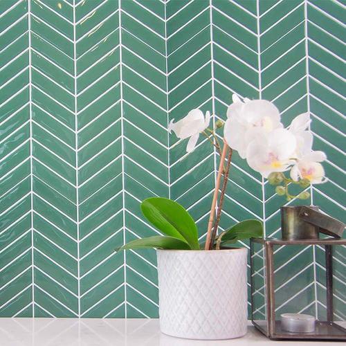 Grønne fliseklistermærker i chevron mønster i bryggers med hvid bordplade pyntet med blomst og stearinlys.