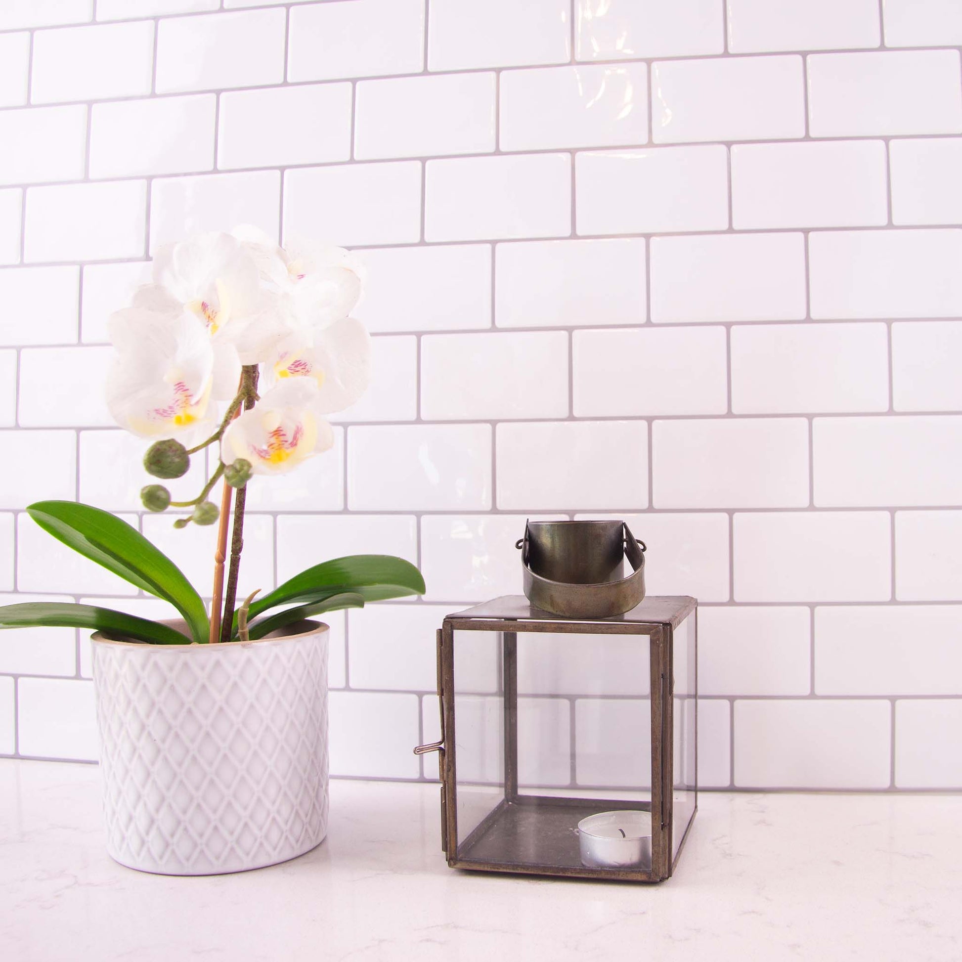 Hvide fliseklistermærker i metro mønster i køkken med hvid marmorbordplade pyntet med blomst og stearinlys.