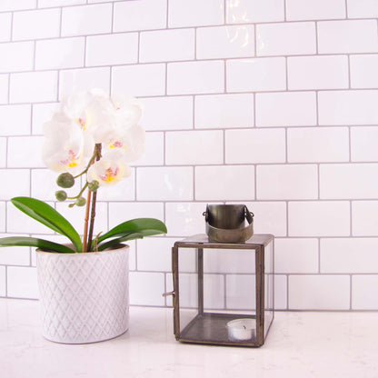 Hvide fliseklistermærker i metro mønster i køkken med hvid marmorbordplade pyntet med blomst og stearinlys.