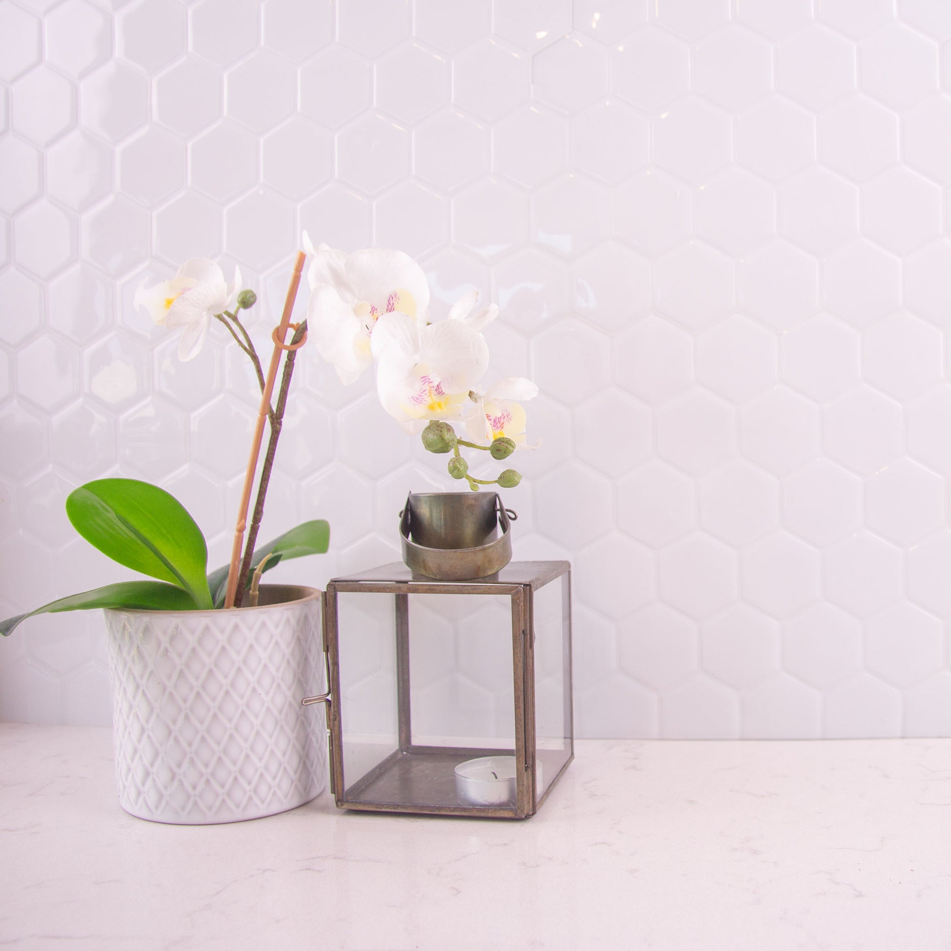 Hvide fliseklistermærker i hexagon mønster (arctic hive) i køkken over lys marmorbordplade.